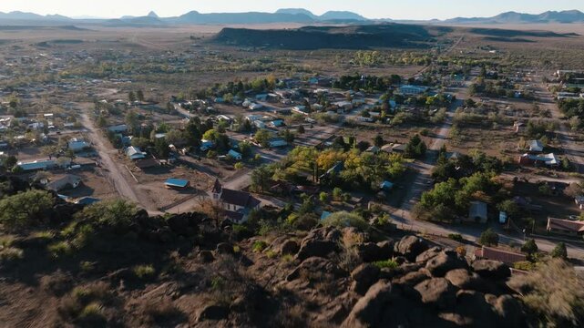 Pulling away to reveal mountaintop overlooking rural Texas Town at Sunrise, Fort Davis in West Texas small town golden hour drone city orbit in 4k