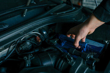 A mechanic's hand replacing a car battery in the engine compartment of a modern vehicle during maintenance. Detailed view of car components and professional work