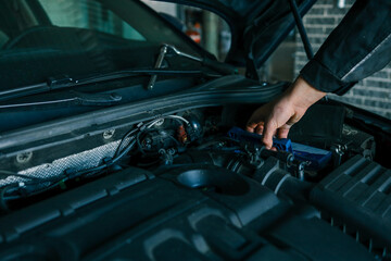 A mechanic's hand replacing a car battery in the engine compartment of a modern vehicle during maintenance. Detailed view of car components and professional work