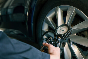 A mechanic checks tire pressure with a gauge during routine car maintenance in a garage. Focus on the wheel and the instrument ensuring optimal vehicle safety and performance