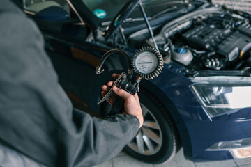 A mechanic holding a tire pressure gauge with a car in the background during vehicle maintenance in...
