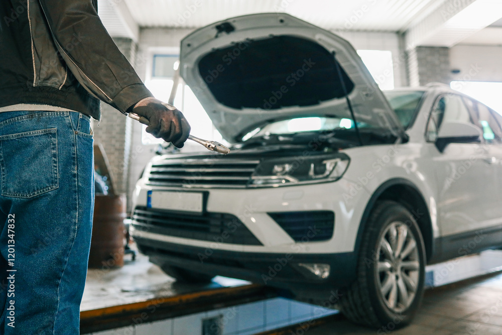 Aufkleber mechanic holding an adjustable wrench in a workshop. a white car with its hood open is visible in th