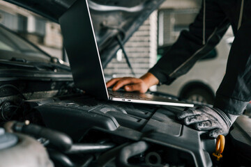 A mechanic using a laptop on a car engine for diagnostics in a garage. Highlights the use of...
