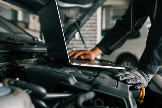 A mechanic using a laptop on a car engine for diagnostics in a garage. Highlights the use of technology in modern vehicle maintenance and repair - Powered by Adobe