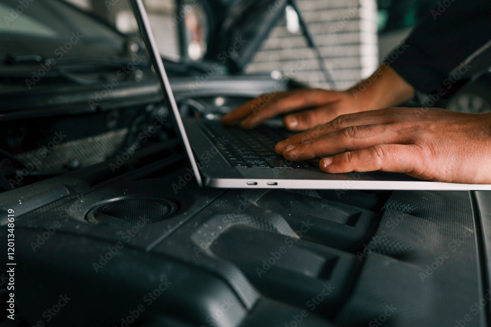 Poster Close-up of a mechanic's hands typing on a laptop placed on a car engine in a workshop, showcasing the integration of technology in vehicle diagnostics and repairs