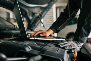 A mechanic using a laptop on a car engine for diagnostics in a garage. Highlights the use of...