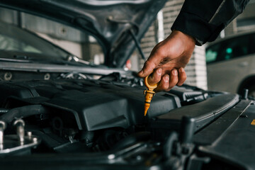 Close-up of a mechanic's hand holding an oil dipstick, checking engine oil levels in a vehicle's open hood. Represents routine car maintenance and servicing