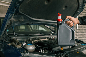 Close-up of a mechanic holding a bottle of motor oil and an oil dipstick, performing an oil change in a vehicle. Highlights car maintenance and servicing tasks