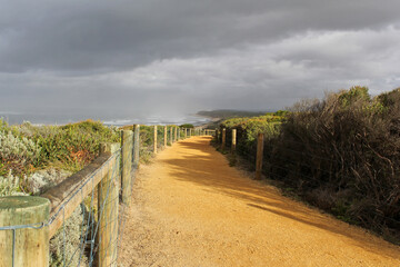 Sandy path bordered by a wooden fence and vegetation at Barwon Heads Bluff in Victoria, Australia