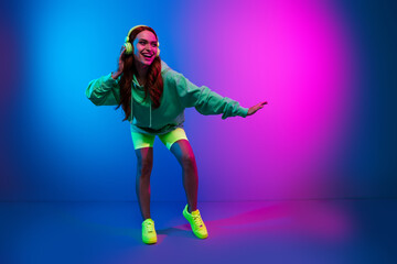 Fototapeta premium Full length photo of shiny attractive lady dressed green sweatshirt earphones enjoying disco empty space isolated blue light color background