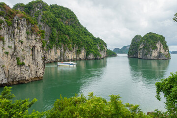 Fototapeta premium A peaceful view of Ha Long Bay with lush cliffs and a boat in the calm water, offering a serene landscape.