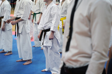 A close-up of a row of young athletes in white karate kimonos with clenched fists and the referee...