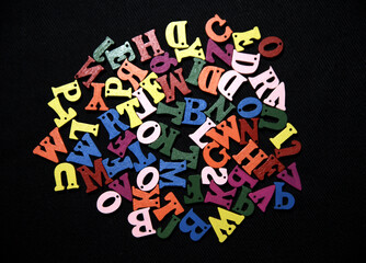Random scattered and colorful Alphabets on the black cloth background.