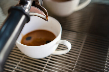 Closeup shot of an espresso maker pouring coffee into a cup inside of a cafe.
