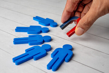 Hand holding a magnet attracts a blue figures. Customer retention concept.