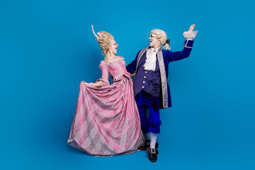 Elegant couple in retro costumes posing playfully against a blue background.