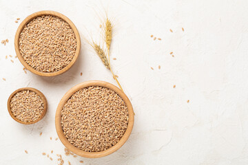 Bowl with spelt grain on concrete background, top view