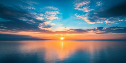 Fototapeta premium Stunning sunrise casting vibrant colors over the sea, with a clear blue sky and fluffy clouds creating a breathtaking landscape. Experience the beauty of sunrise over the tranquil sea.