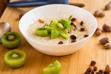 cooked oatmeal with kiwi, honey and nuts in a bowl on a wooden table