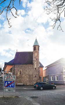 Achern, Germany - Jan 3, 2025: A medieval-style church in Achern, Germany, featuring a tall stone tower under a bright sky, surrounded by traffic signs and nearby urban buildings.