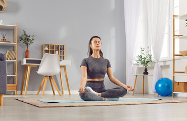 Portrait of a relaxed young woman doing yoga exercise sitting on the floor in lotus pose. Caucasian...
