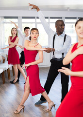 Fototapeta premium Smiling young woman and African american partner successfully perform mesmerizing movements of paso doble dance during celebration or party
