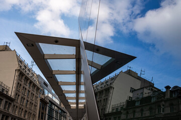 An artistic viewpoint of a sleek urban rooftop structure with a glass canopy showing reflections of the surrounding buildings and the sky, highlighting modern architectural elements in London UK