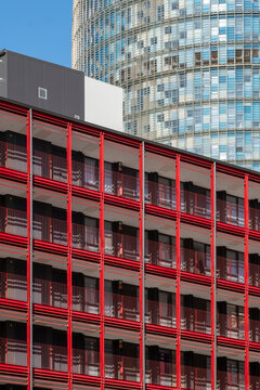 This image showcases a vibrant red building facade with multiple balconies set against a backdrop of contemporary skyscrapers, highlighting urban architectural contrast  in Barcelona Spain