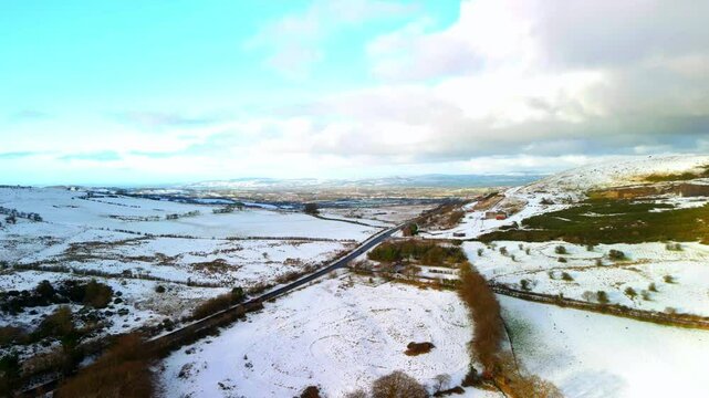 Aerial shot of Cavehill in Belfast, Northern Ireland on a snowy and calm winter day. The camera rises to reveal snow covered mountains and fields. Shot in 4K, 60fps and in Rec709 color.