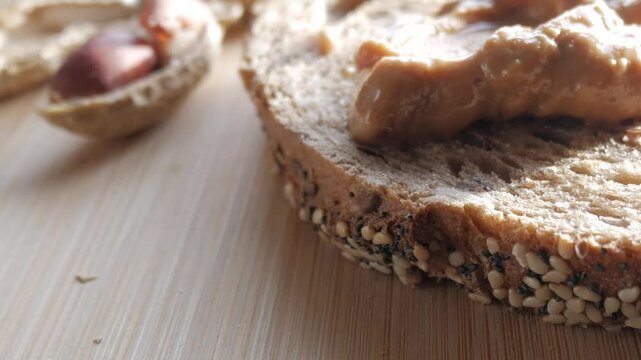A slice of multigrain bread topped with creamy peanut butter on a wooden surface
