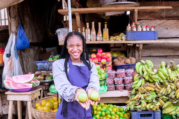 Female market vendor wearing an apron smiling brightly while showcasing fresh produce at her colorful market stall. The vibrant fruits and vegetables create a welcoming and cheerful atmosphere.