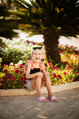 Naklejka premium Happy little girl laughing among palm trees on vacation