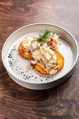 A gourmet dish featuring two golden cornbread slices topped with creamy mushroom sauce, shredded chicken, and garnished with herbs. Presented on a minimalist white plate against a wooden background.