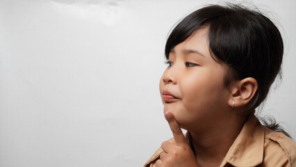 Portrait of an Asian girl with a white background wearing a scout uniform and tied hair with a pensive expression while frowning and holding her chin with one hand.