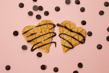 Heart shaped cookies with melted chocolate and sprinkles scattered on a pink background. Valentine's Day concept