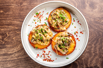 Deliciously plated mini savory cakes topped with sautéed mushrooms and onions, garnished with fresh herbs and chili flakes, served in a white dish on a wooden table.