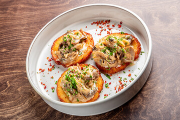 Deliciously plated mini savory cakes topped with sautéed mushrooms and onions, garnished with fresh herbs and chili flakes, served in a white dish on a wooden table.