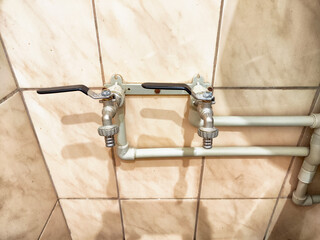 Two plumbing taps connected to pipes on a tiled wall in a utility space showcasing pipes and fixtures