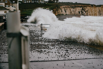 A large wave is crashing into the shore, and the water is filled with debris