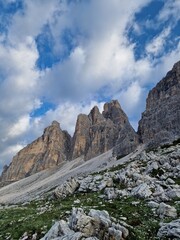 Stunning view of rugged mountain peaks in the Dolomites,  sharp, jagged shapes and rocky surfaces, lush green grass, fluffy clouds, hiking path to Tre Cime di Lavaredo