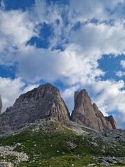 Stunning view of rugged mountain peaks in the Dolomites,  sharp, jagged shapes and rocky surfaces, lush green grass, fluffy clouds, hiking path to Tre Cime di Lavaredo