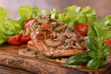 Chicken breast with mushroom sauce and vegetables on a wooden plate