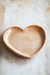 A heart-shaped plate made from natural clay sits on a light wooden table. The matte finish and organic texture enhance its rustic charm, offering ample space for creative text overlay