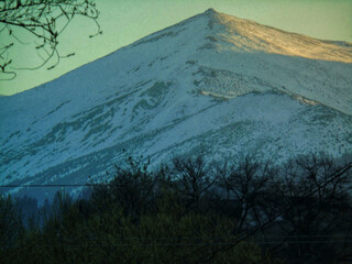 A snow-capped mountain peak at sunset seen from a village
