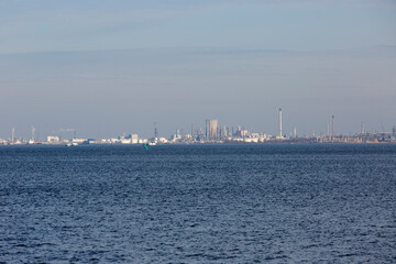 City skyline viewed from the water on a clear day, showcasing industrial structures and wind turbines in the distance