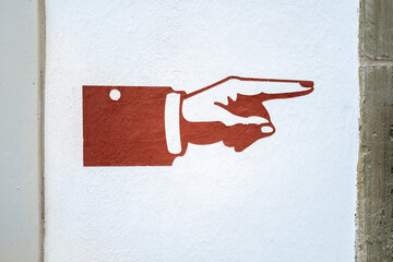 Brown hand pointing right is painted on a white wall. The simple design serves as a clear directional indicator. 