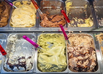 A variety of colorful gelato flavors are displayed in metal containers. 