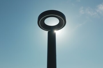 Modern circular street lamp standing tall against a clear blue sky, sun shining brightly behind it