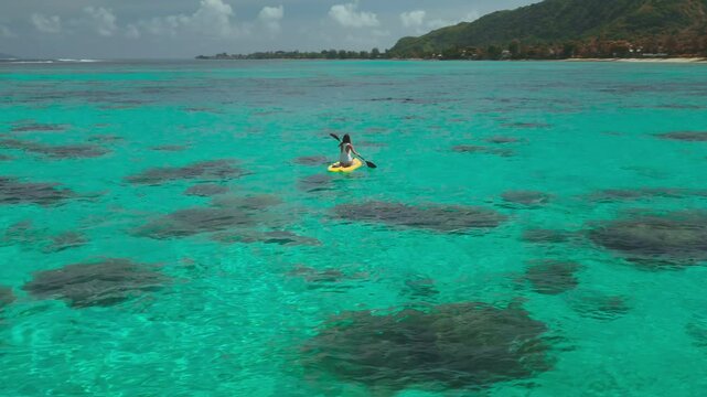 Woman paddleboarding on a yellow board in turquoise waters around a tropical island, enjoying the sun and feeling free