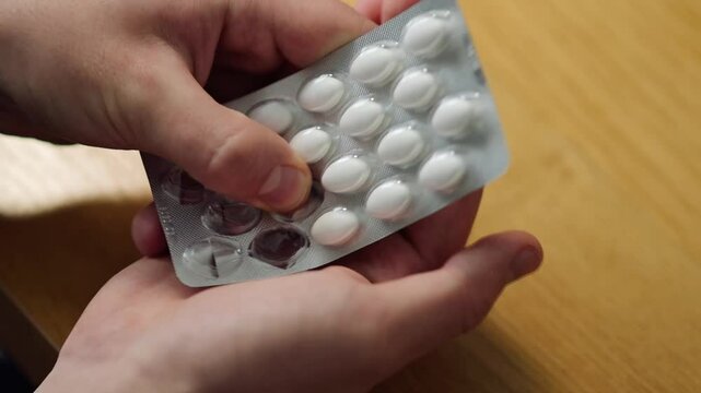 A person unpacking a white pill and preparing to take it